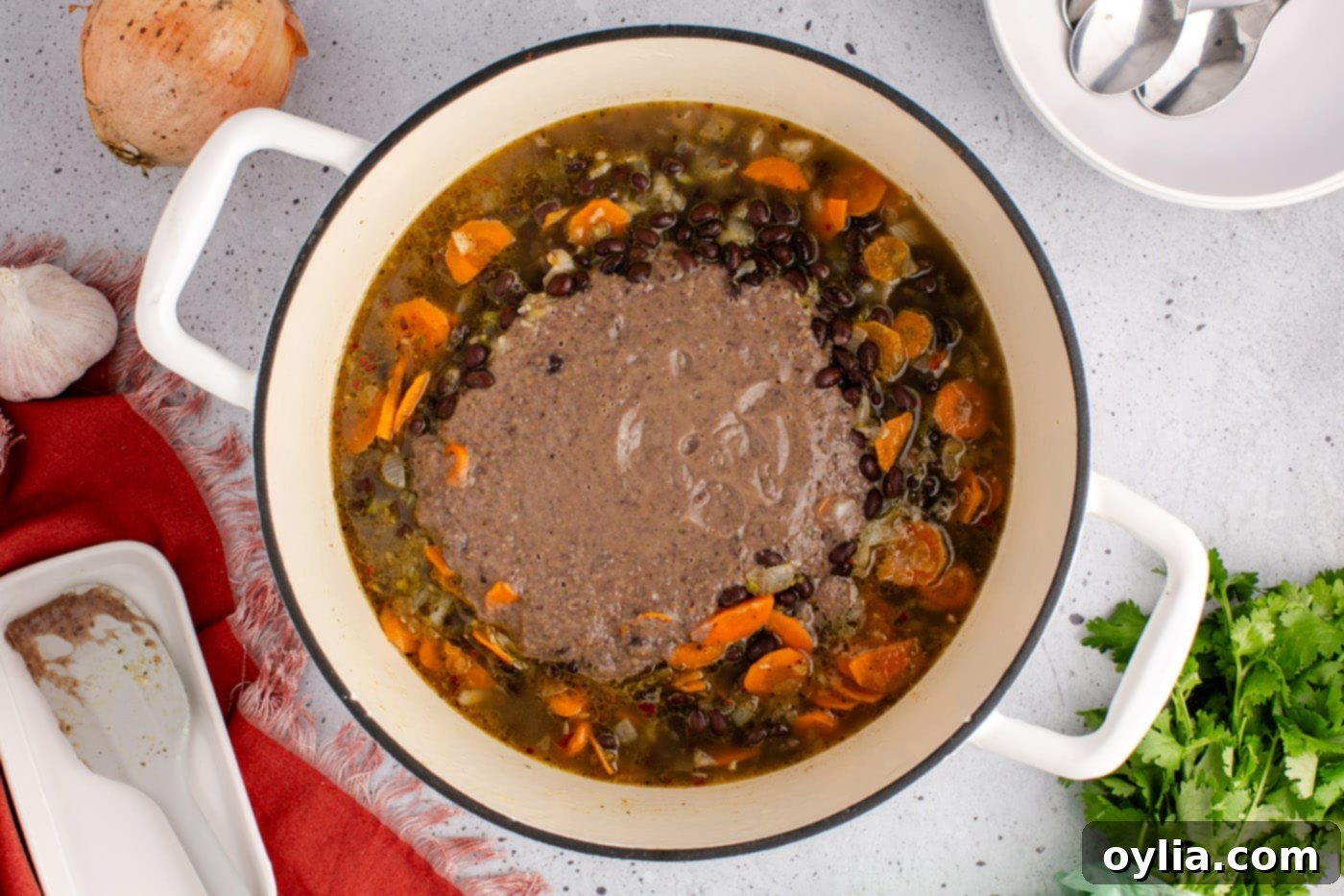 Adding blended black bean soup back to the non-blended soup in the pot, combining for a uniform texture.