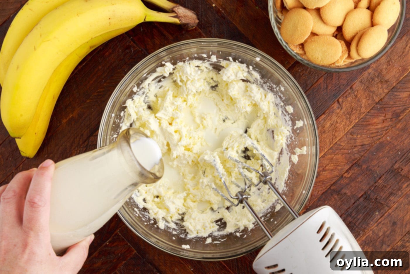 adding whole milk to whipped cream cheese in a bowl with a mixer