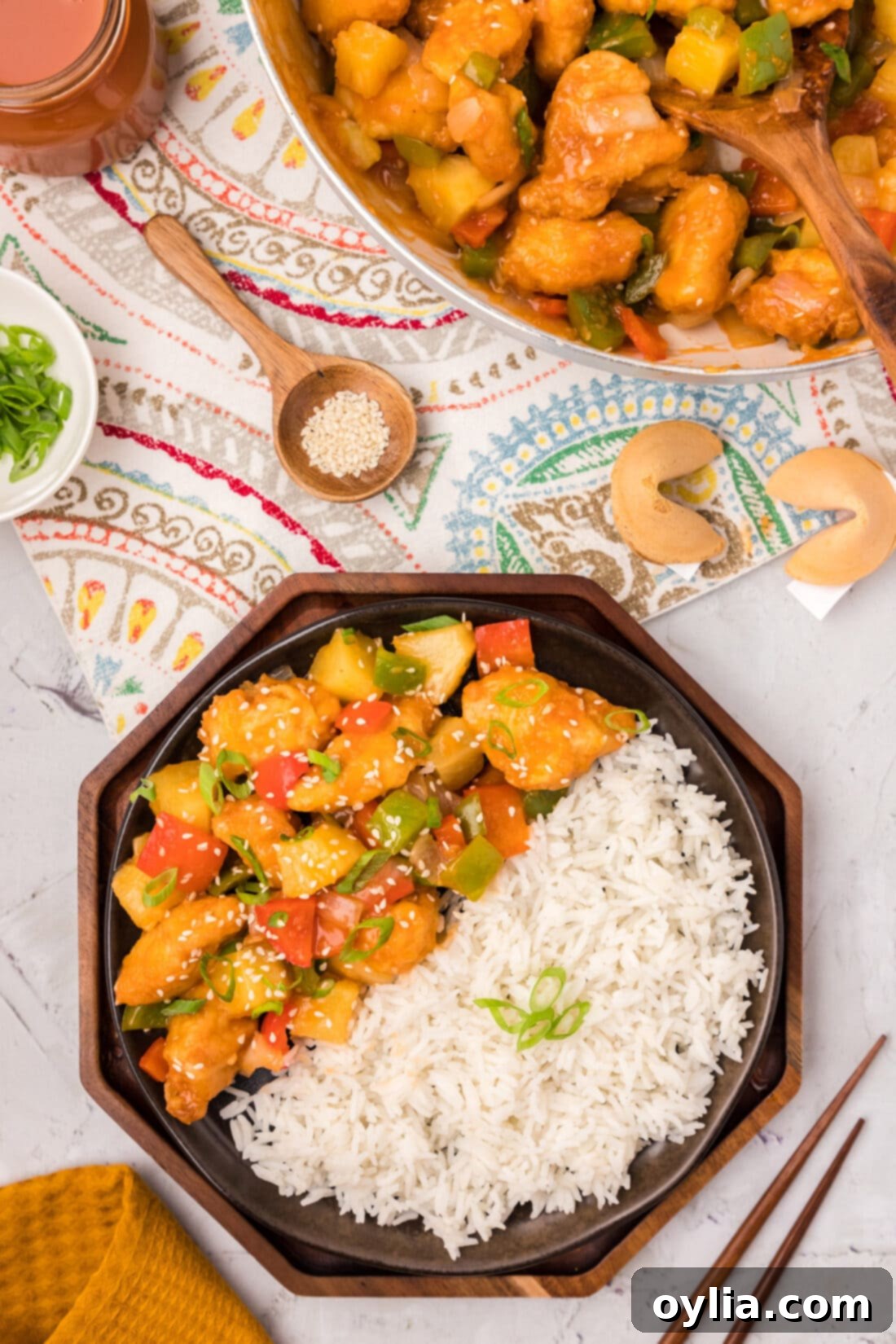 Plate of Sweet and Sour Chicken with rice on the side, garnished with green onions and sesame seeds.