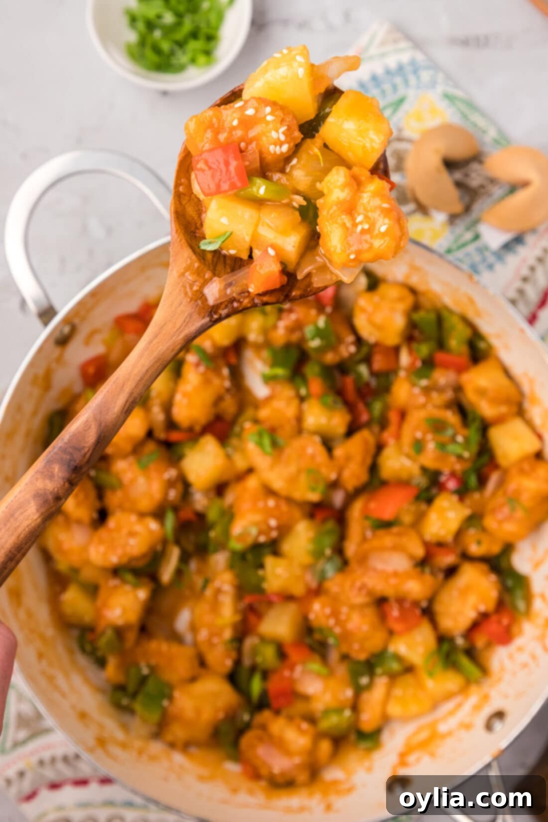 Spoonful of Sweet and Sour Chicken held above a skillet of Sweet and Sour Chicken, showcasing the vibrant colors and glossy sauce.