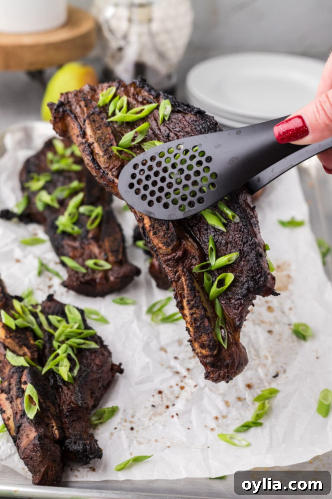 Tongs holding up a Korean Short Rib, showing its perfect char and tenderness after grilling.