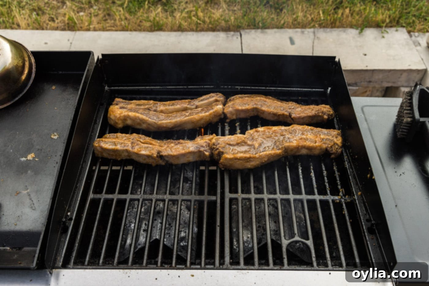 Korean barbecue short ribs searing on a hot grill, showing the early stages of cooking and charring.