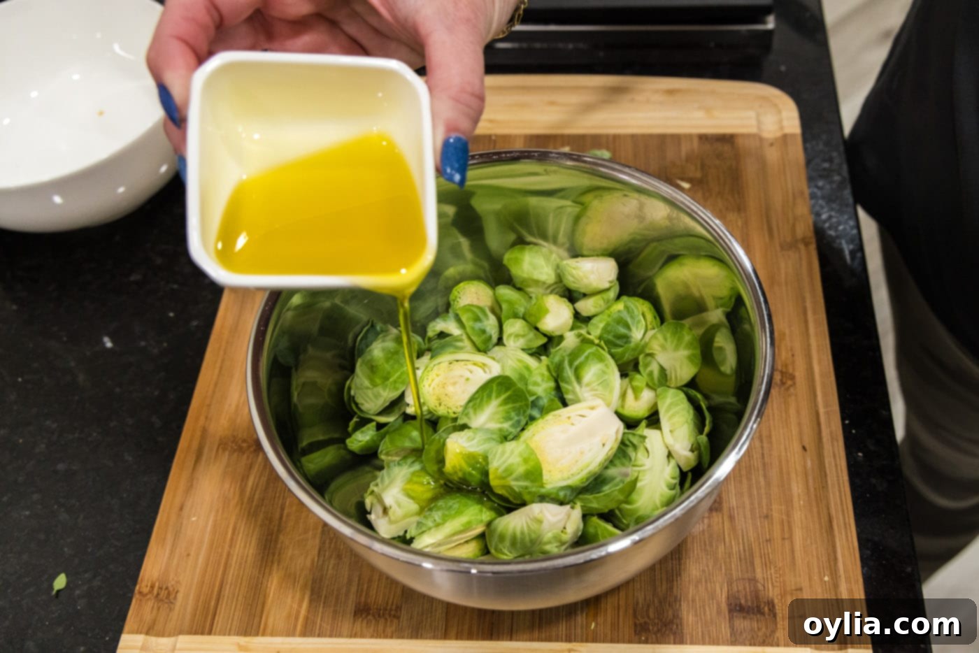adding olive oil to bowl of brussels sprouts