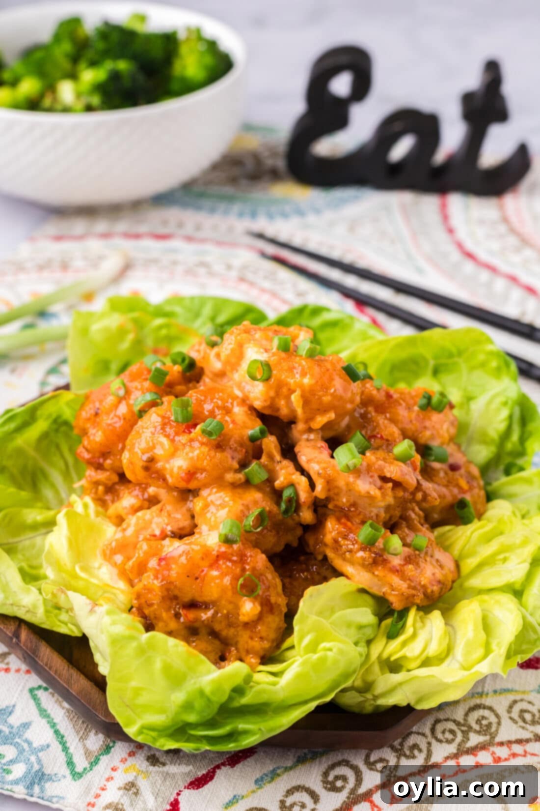 Bang Bang Shrimp on a bed of lettuce with a bowl of broccoli in the background