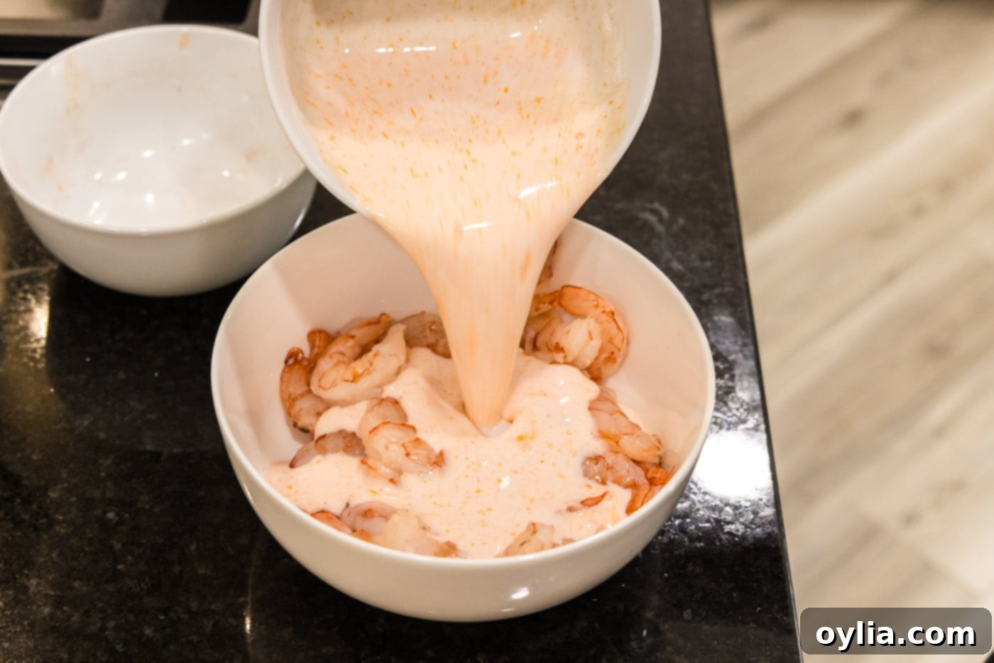 pouring buttermilk hot sauce mixture over shrimp in a bowl