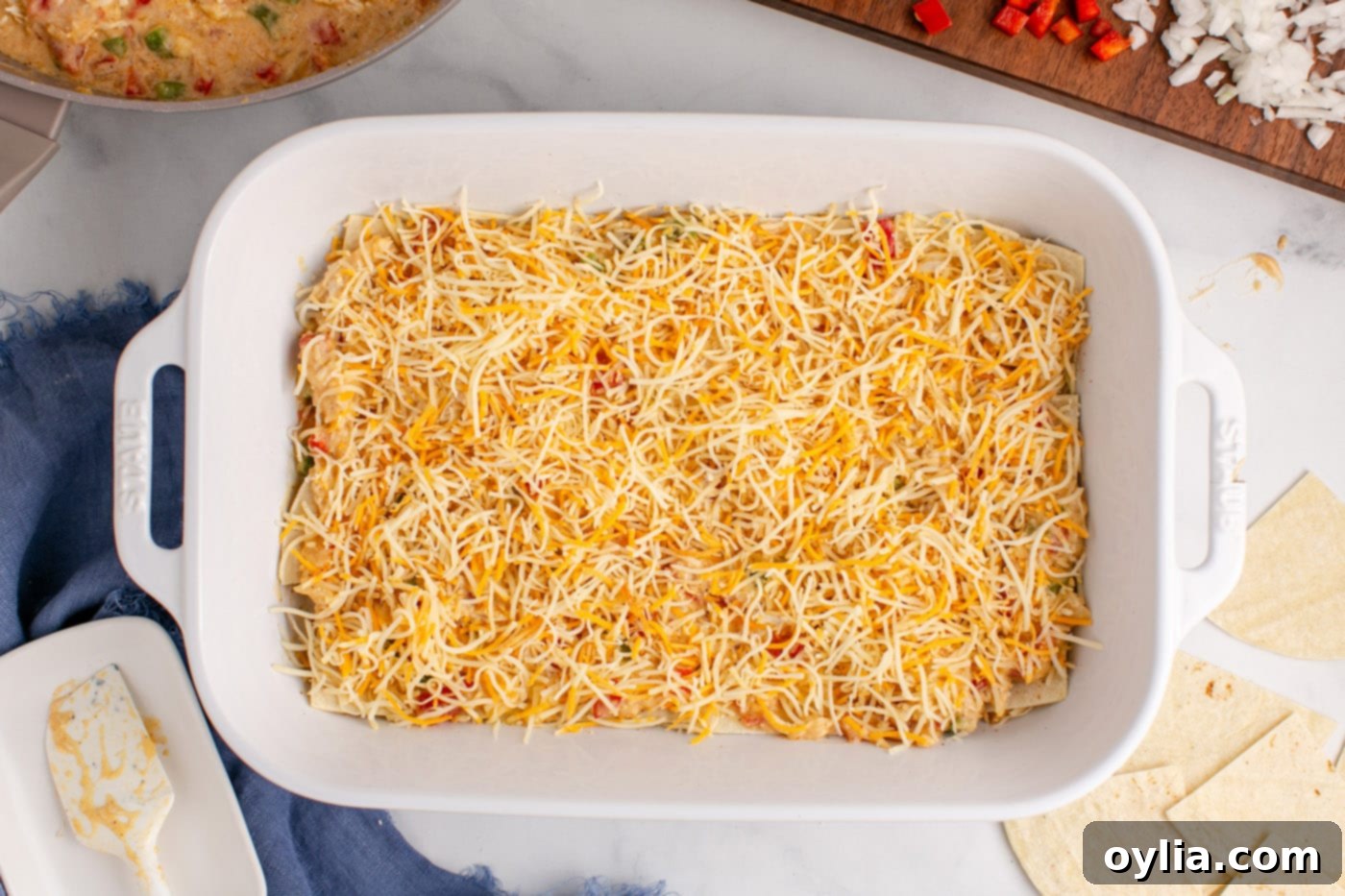 shredded cheese layered over chicken sauce in a baking dish