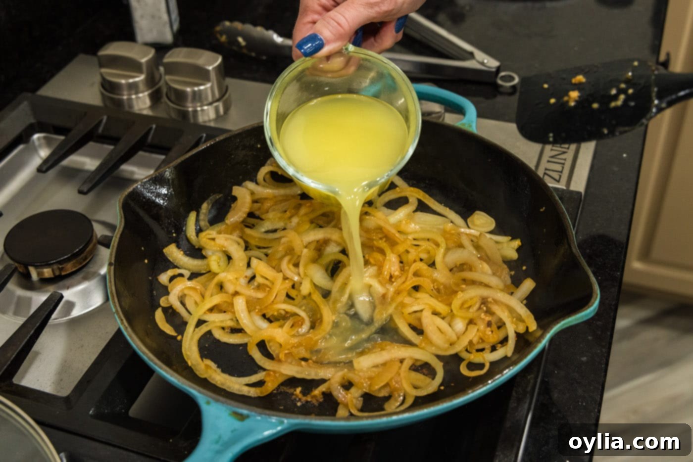 pouring chicken broth into skillet with onions