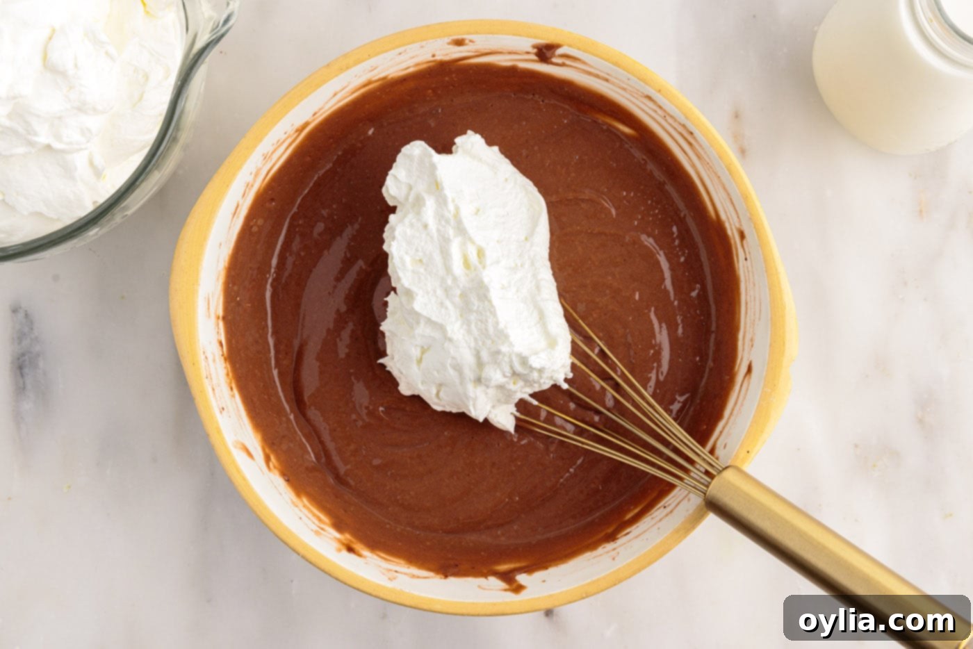 adding whipped cream to chocolate pudding in a bowl