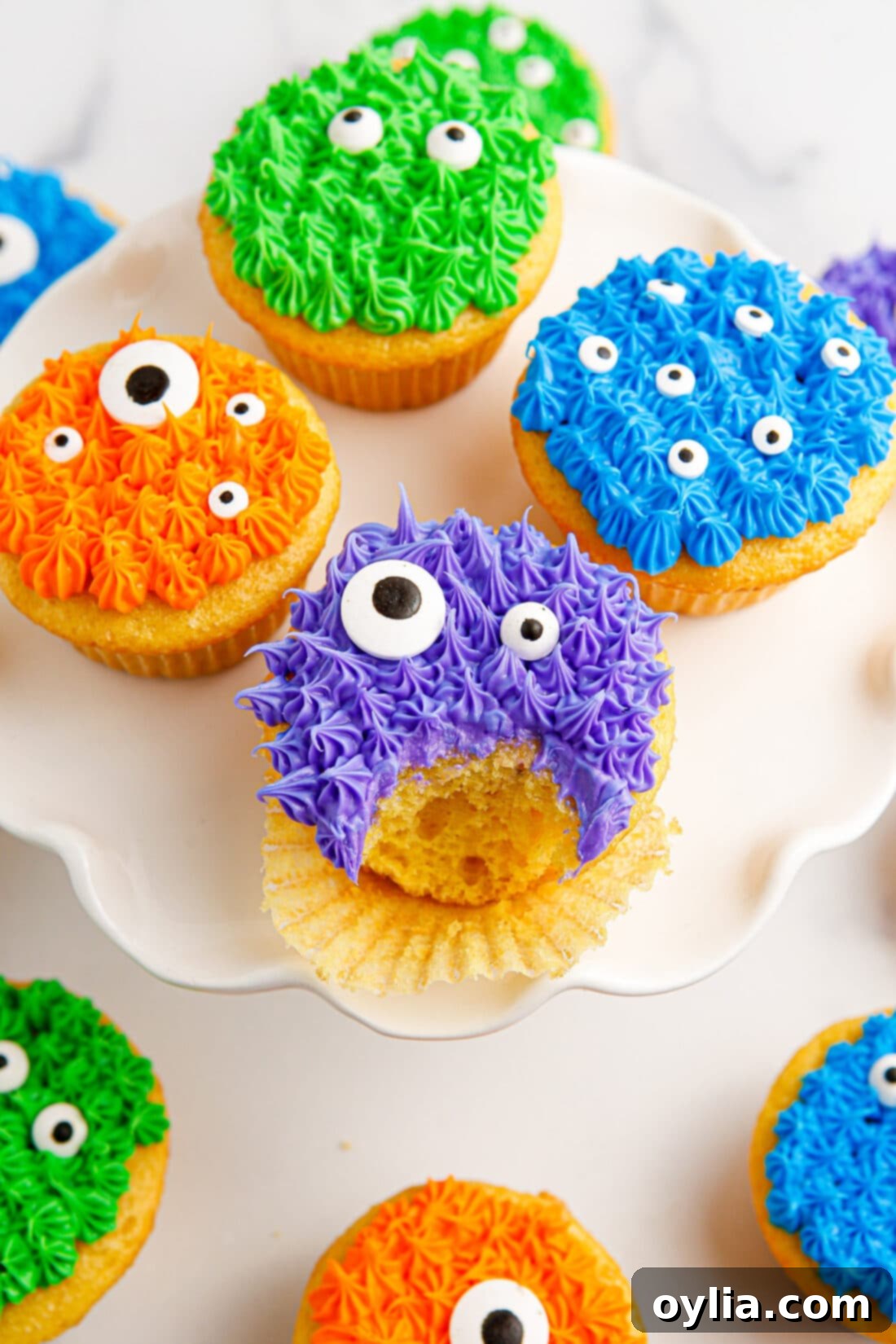 Monster Cupcakes on a cake stand with a bite taken out of one, showcasing colorful frosting and candy eyes.