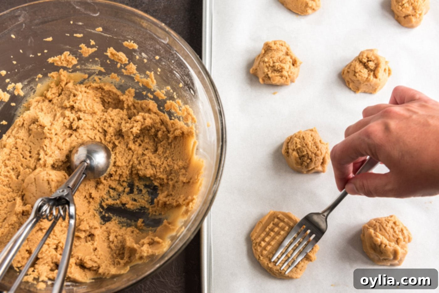 A fork being used to create the classic crisscross pattern on raw peanut butter cookie dough balls on a baking sheet.