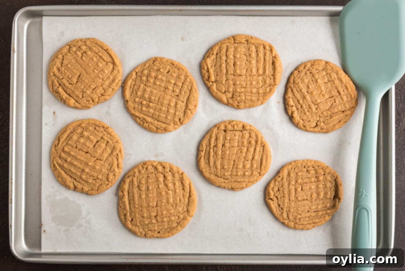 Freshly baked peanut butter cookies on a baking sheet, golden brown and ready to cool.