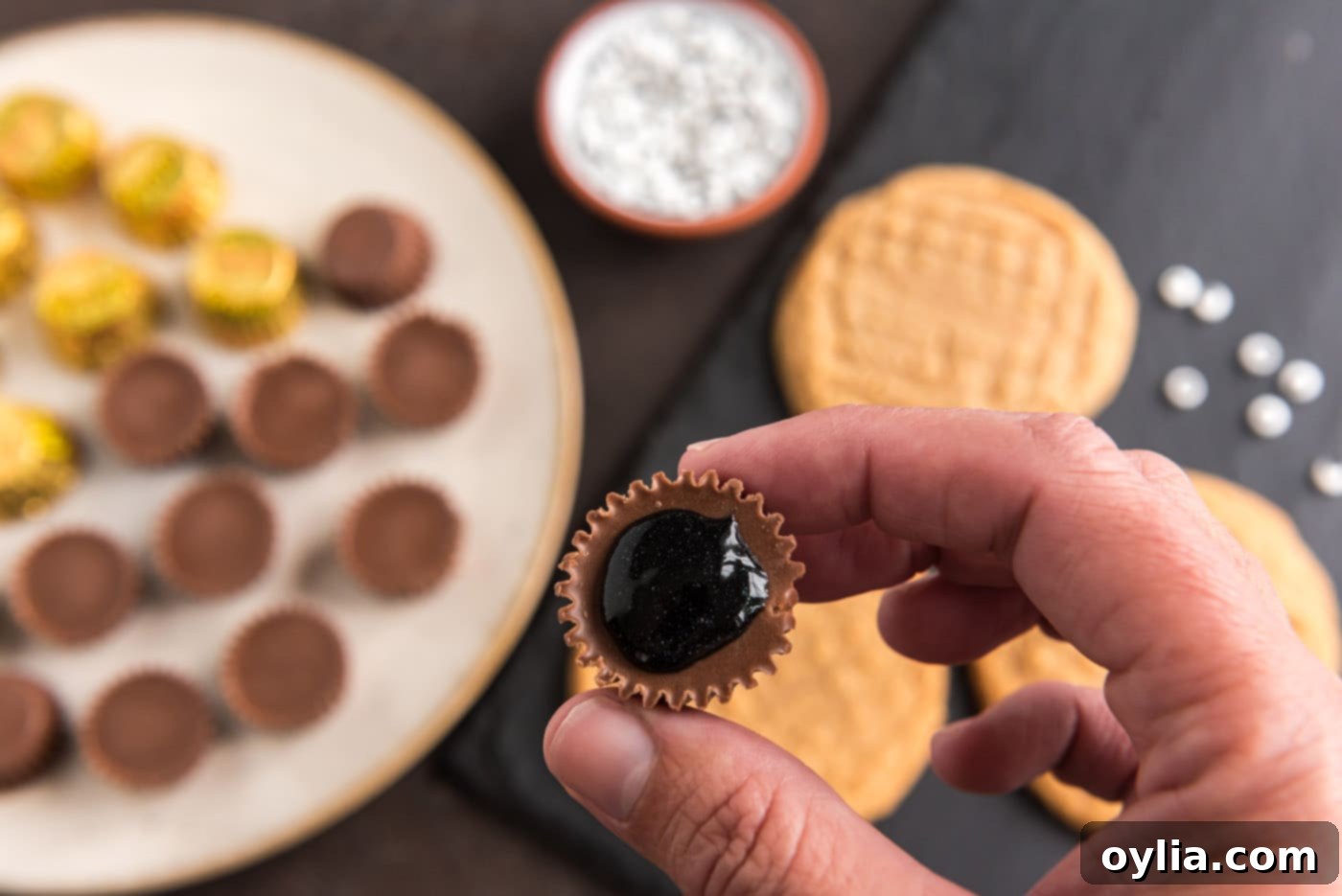 A mini Reese's peanut butter cup with a dot of black decorator gel on its base, ready to be attached to a cookie.