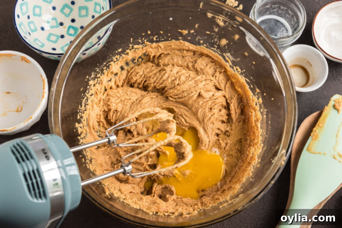Adding an egg to the mixed wet ingredients for peanut butter cookie dough, being blended with an electric mixer.
