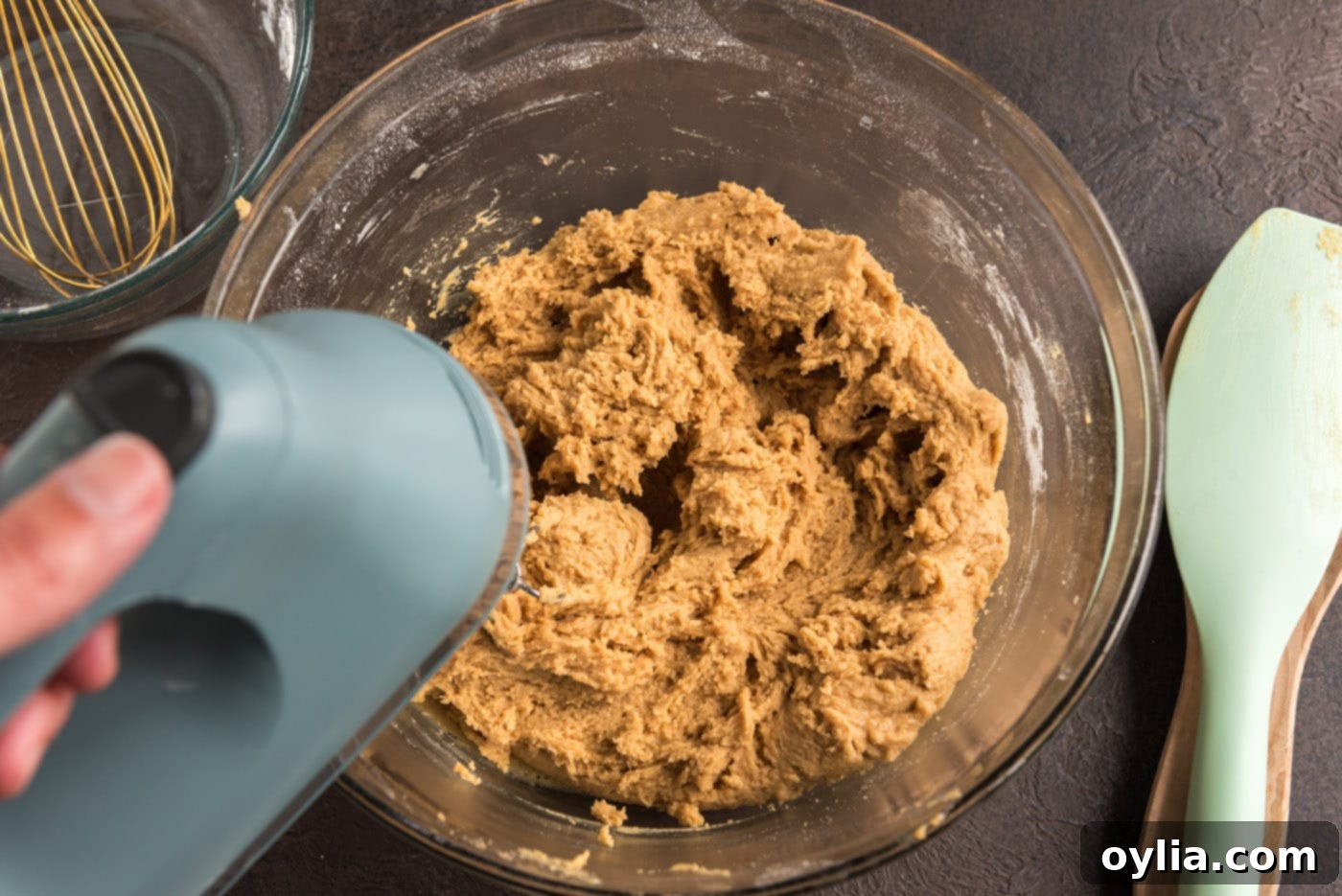 Electric mixer blending the dry and wet ingredients into a smooth peanut butter cookie dough.