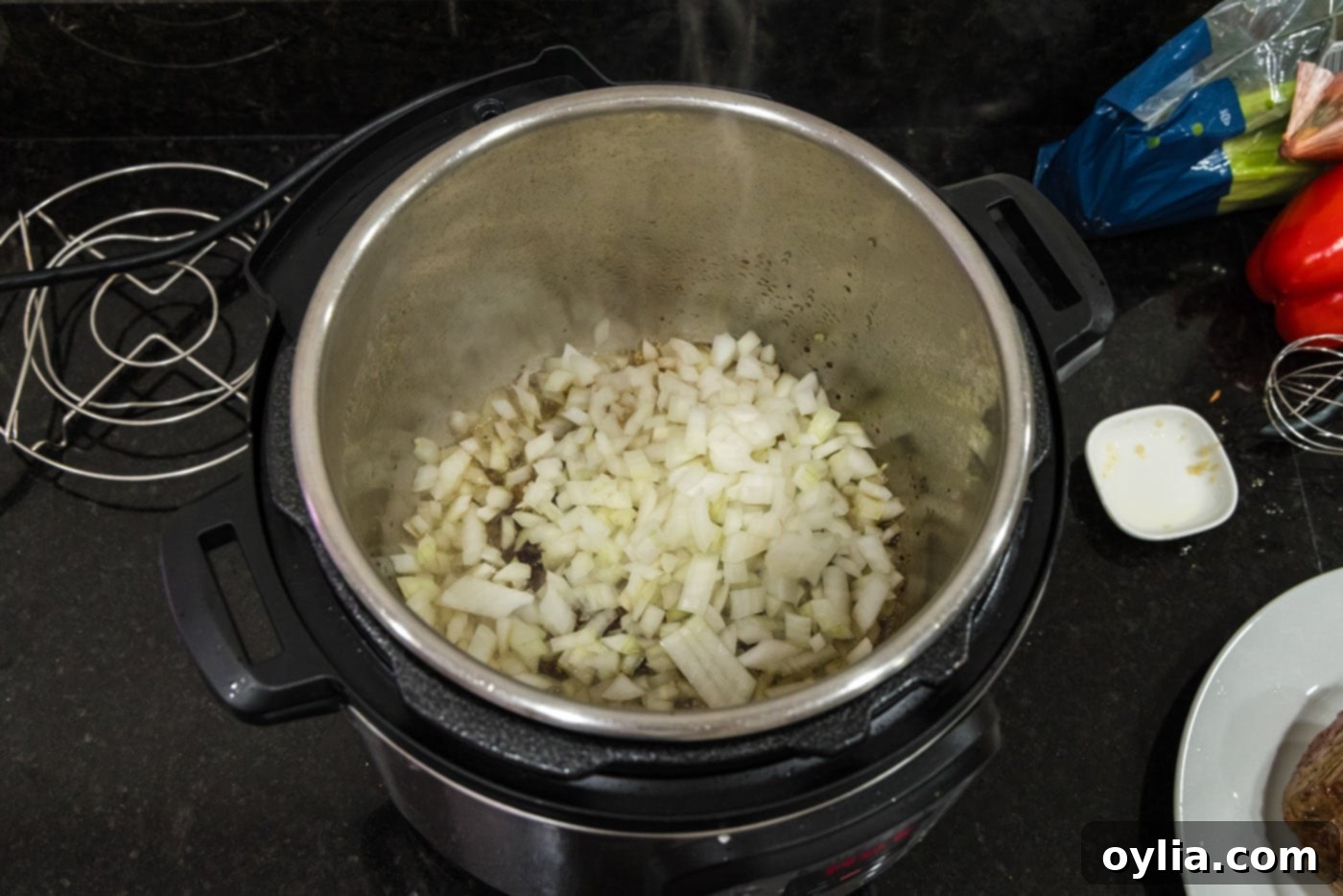 Chopped onion and minced garlic being sautéed in the Instant Pot with residual pan juices, creating an aromatic base for the roast.