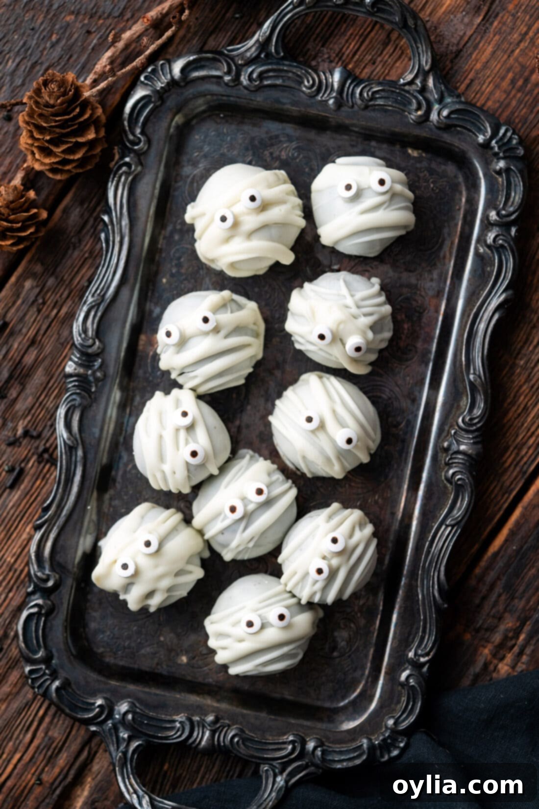 Mummy Oreo Truffles on a black tray, decorated with white chocolate 'bandages' and candy eyes, evoking a spooky yet cute Halloween theme.