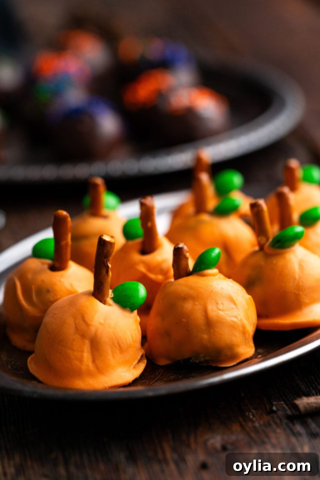 Close up photo of pumpkin oreo truffles on a platter, featuring bright orange coating, pretzel stems, and green M&M 'leaves'.