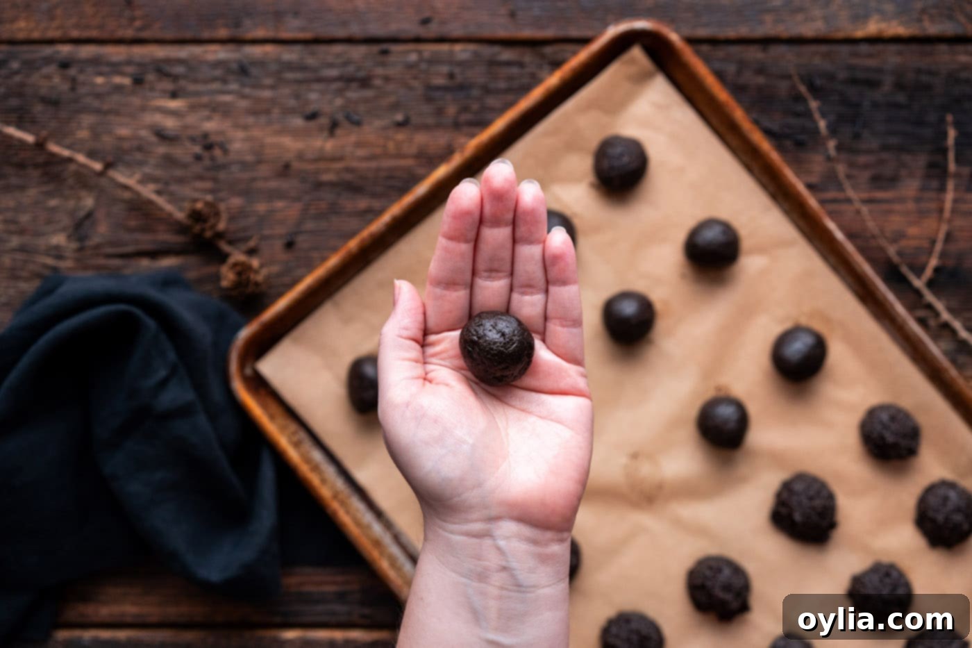 A hand shaping a scooped Oreo truffle mixture into a perfectly round ball.