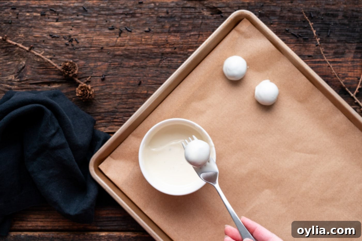 Dipping an Oreo truffle into melted white chocolate, ensuring a full and even coating.