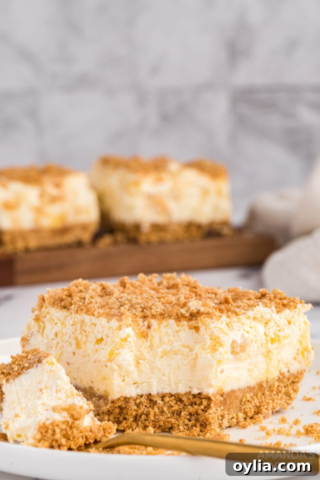 A perfectly portioned slice of Pineapple Dream Dessert with a bite taken, showcasing its creamy layers and graham cracker crust.