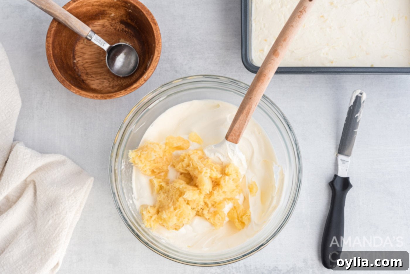 Crushed pineapple being folded into a bowl of fluffy Cool Whip for the top layer of the dessert.