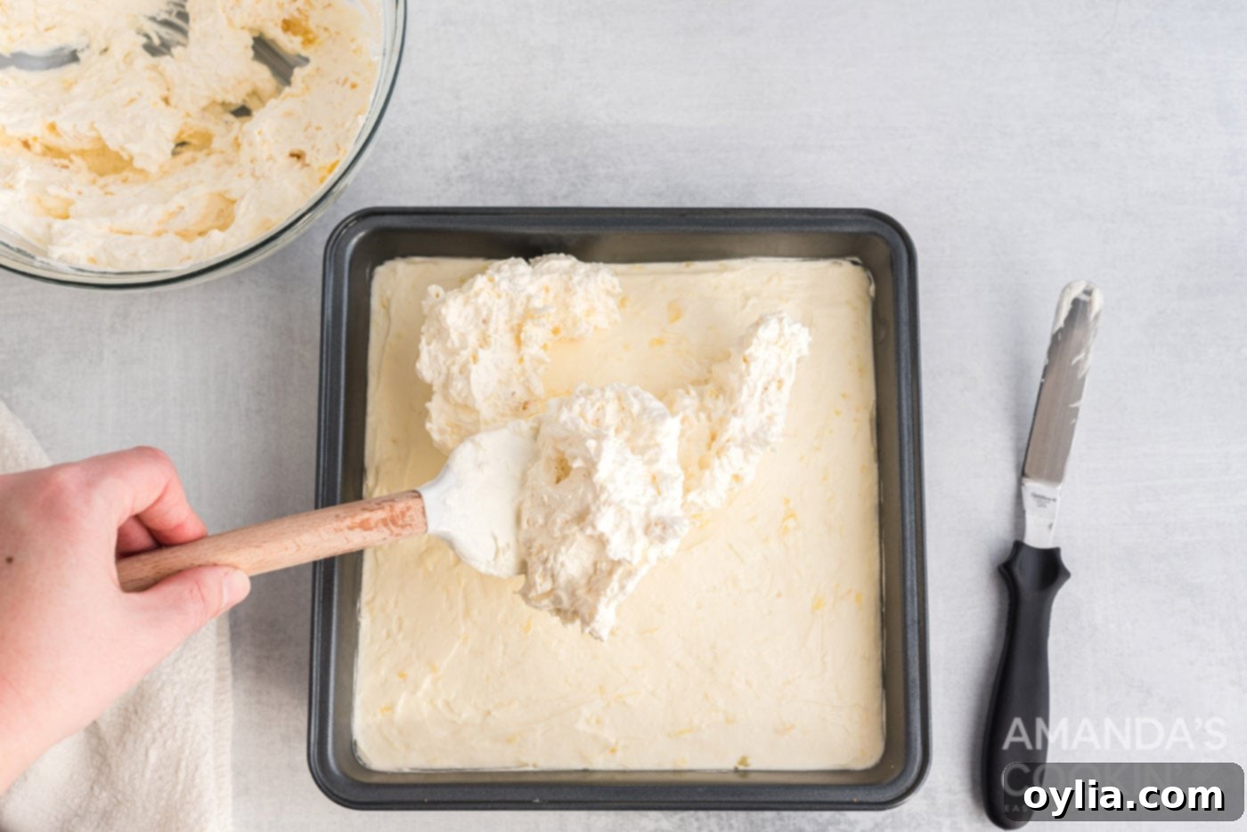 The pineapple-whipped topping mixture being carefully spread over the cream cheese layer in the baking pan.