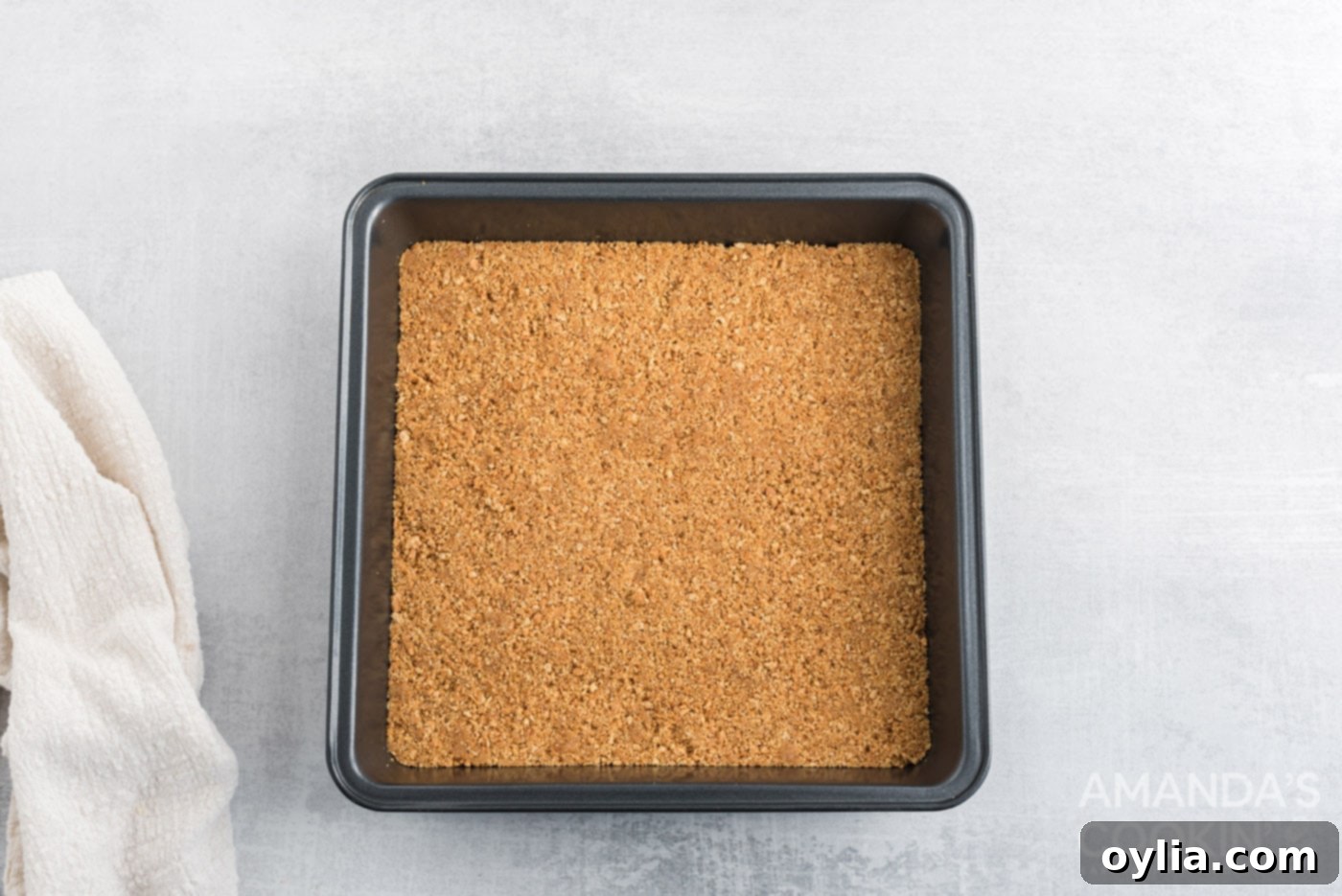 Graham cracker crumb crust firmly pressed into a square baking pan, ready for the oven.