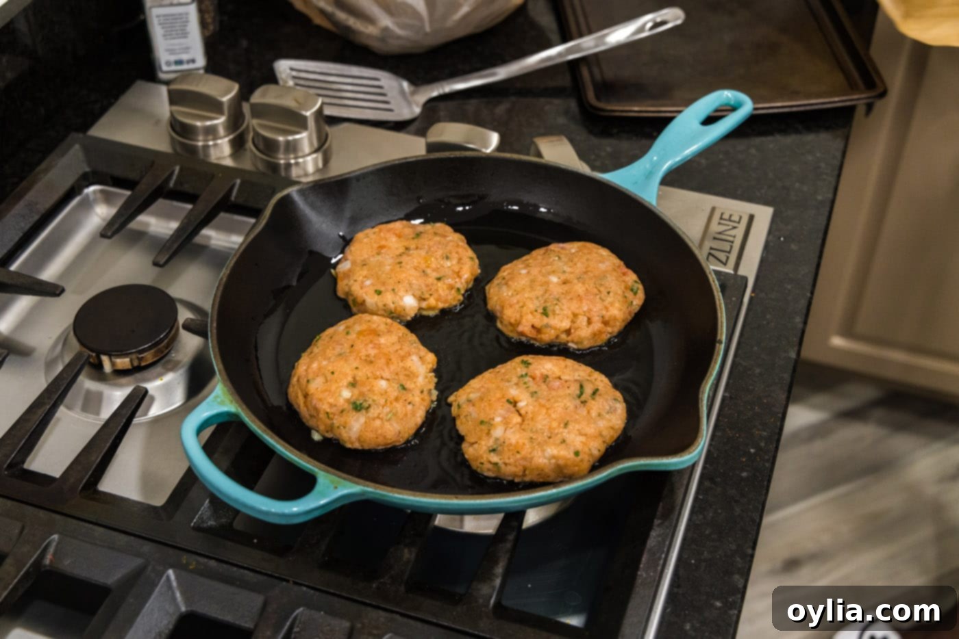 Salmon burgers sizzling and pan-searing to a golden brown in a hot skillet
