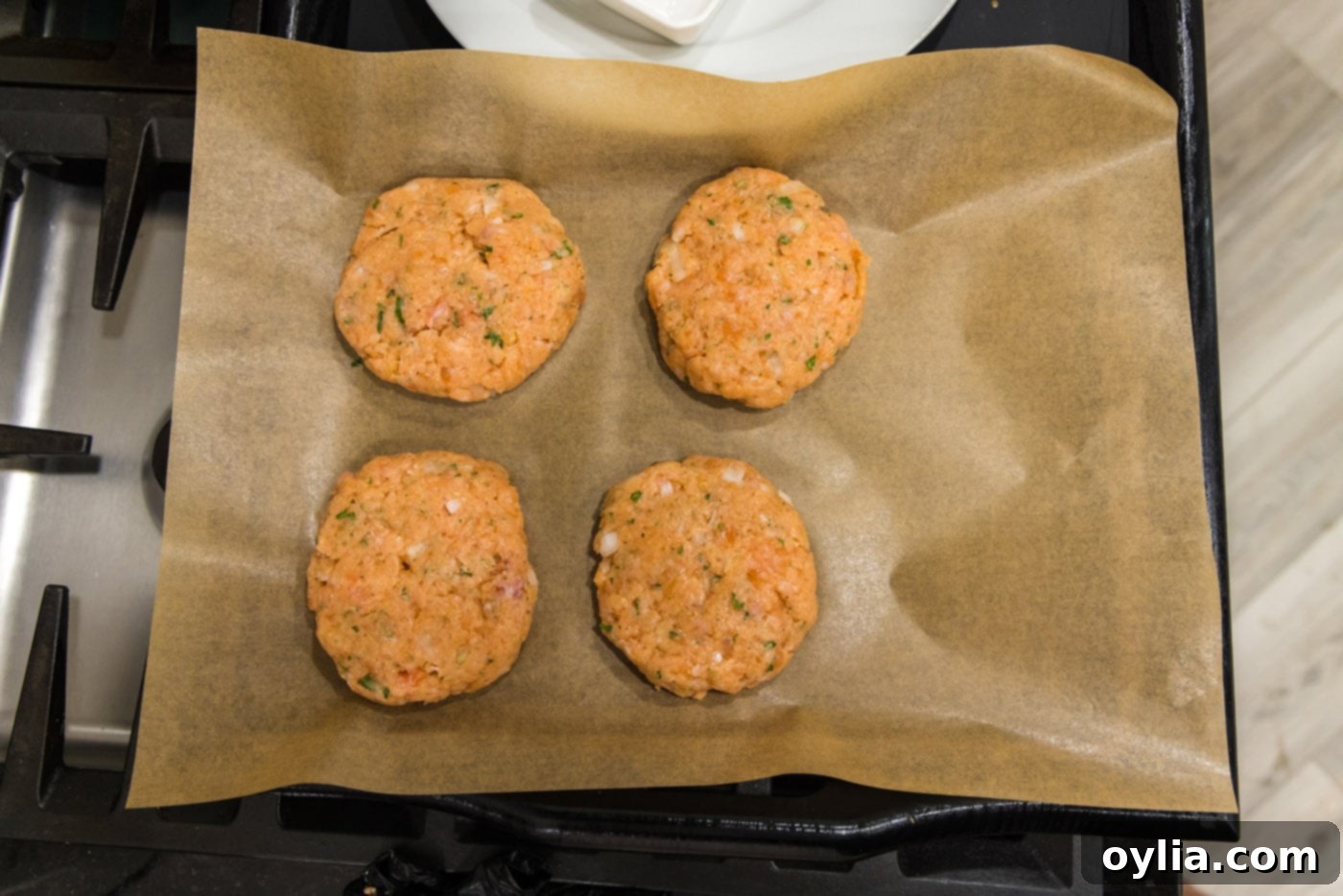 Four raw salmon patties neatly arranged on parchment paper, ready for cooking