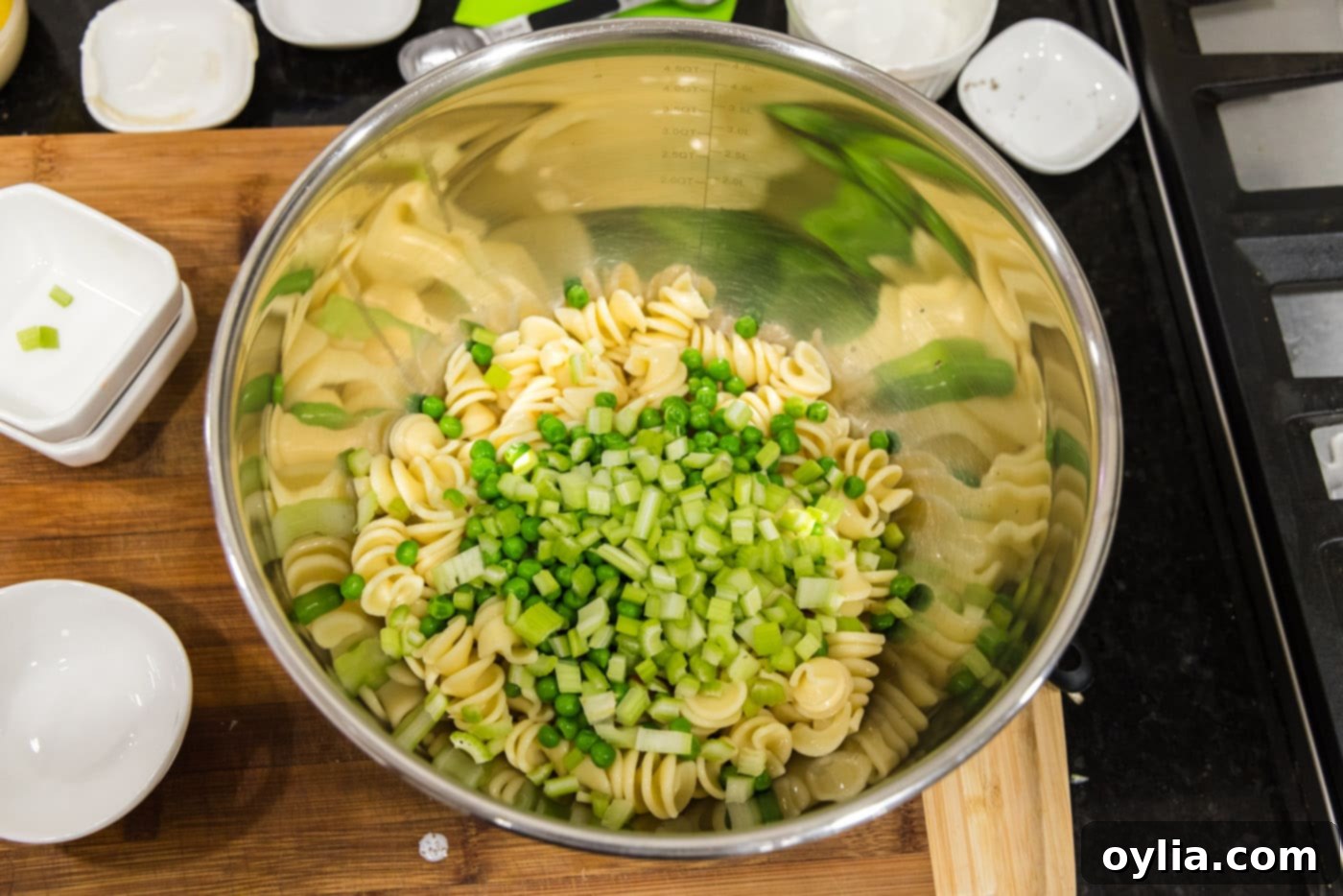 adding chopped celery and peas to bowl with pasta