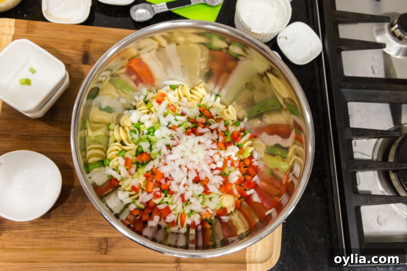 chopped bell peppers and onion added to rotini pasta in a bowl