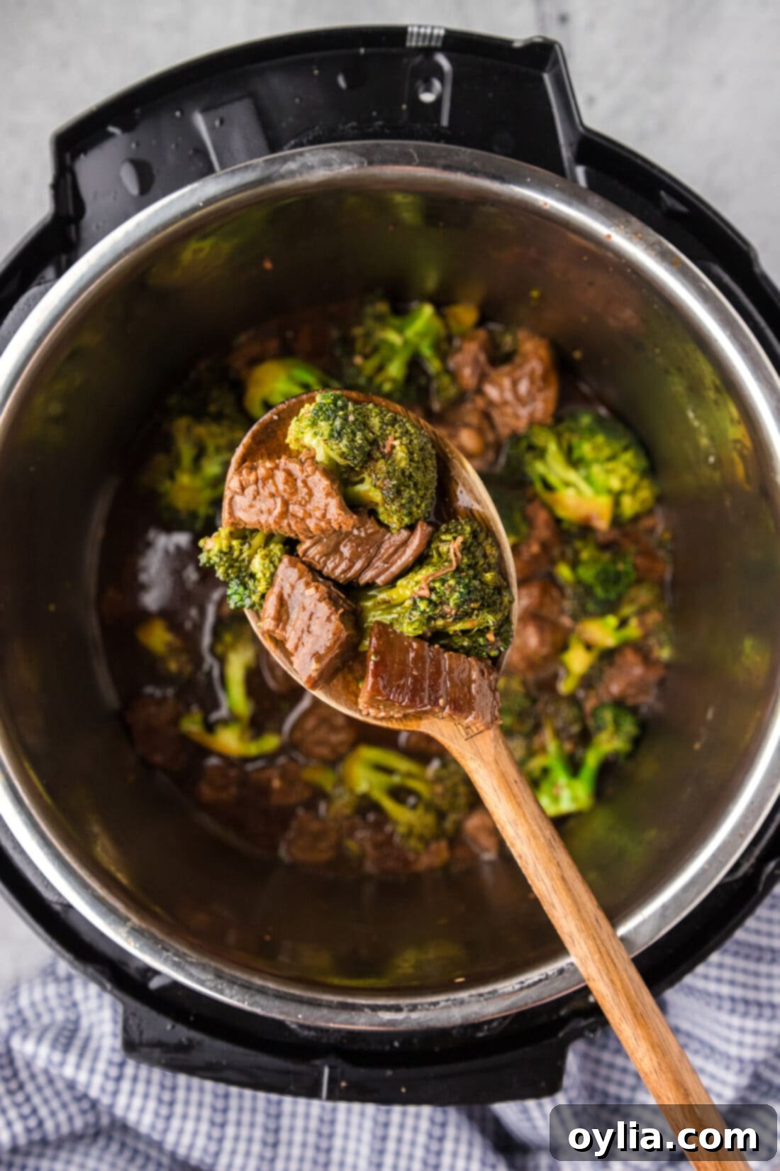 A serving spoon lifts tender Instant Pot Beef and Broccoli from the pot, showcasing the rich sauce and perfectly cooked ingredients.