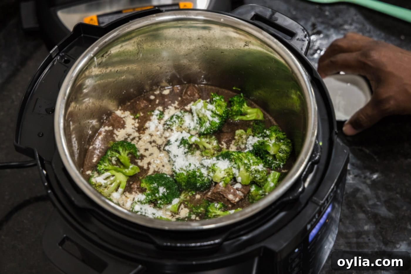 Cornstarch being sprinkled over fresh broccoli florets in the Instant Pot with beef and sauce.