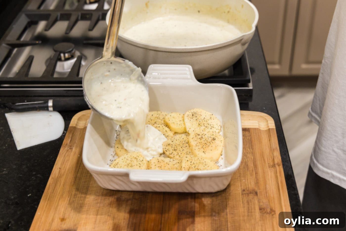 ladeling cream sauce over scalloped potatoes in a dish