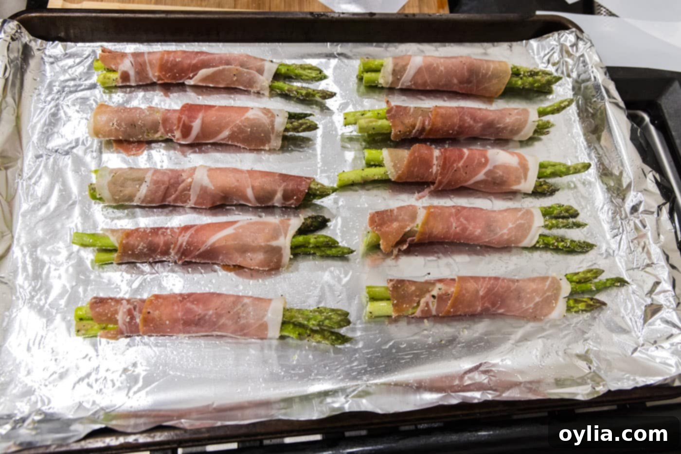 Prosciutto wrapped asparagus arranged neatly on a baking sheet