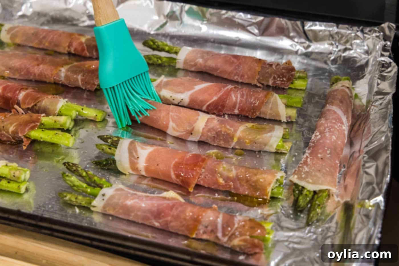 Basting prosciutto wrapped asparagus with leftover olive oil mixture on a baking sheet