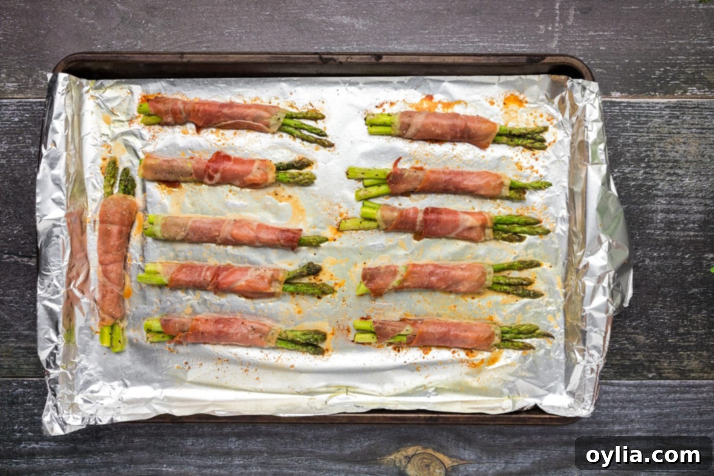 Golden-brown prosciutto wrapped asparagus on a baking sheet, fresh out of the oven