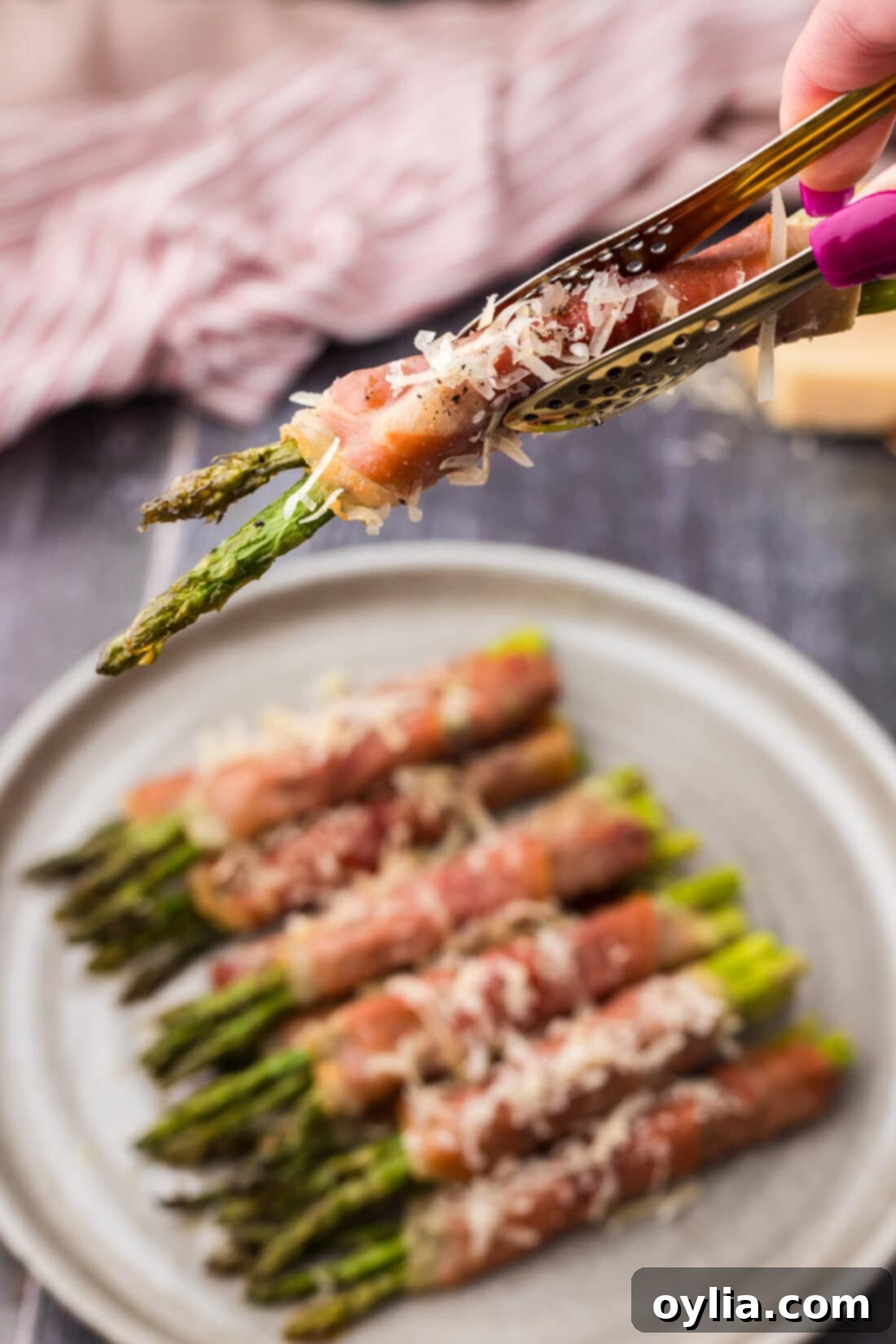 Tongs holding up a single prosciutto wrapped asparagus bundle, perfectly cooked