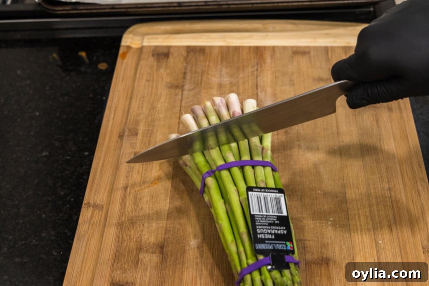 A knife cutting the woody ends off fresh asparagus spears on a cutting board