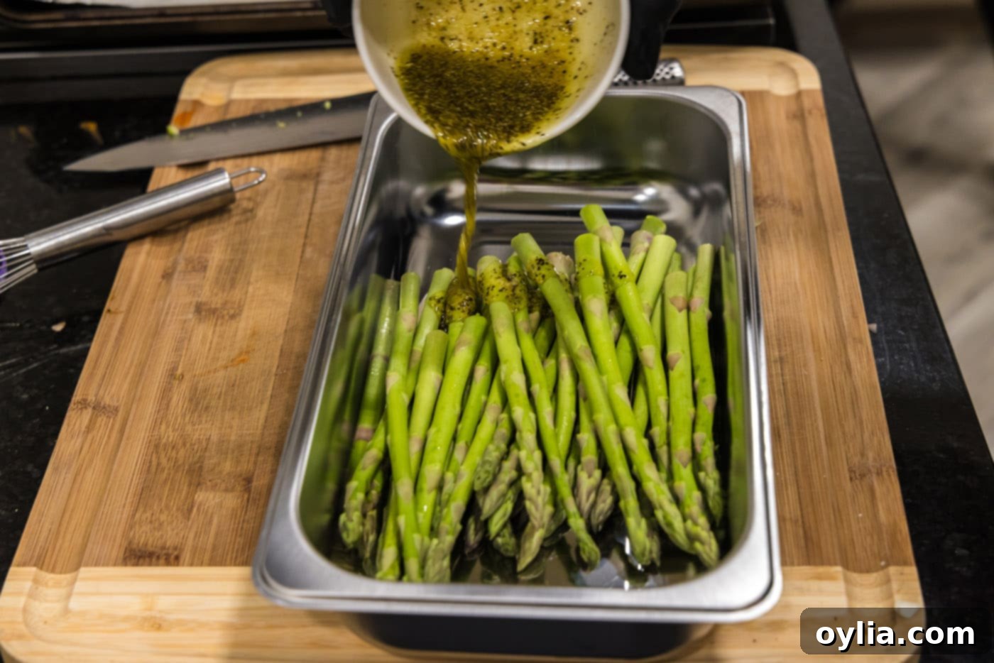 Pouring olive oil and seasoning mixture over asparagus spears in a bowl