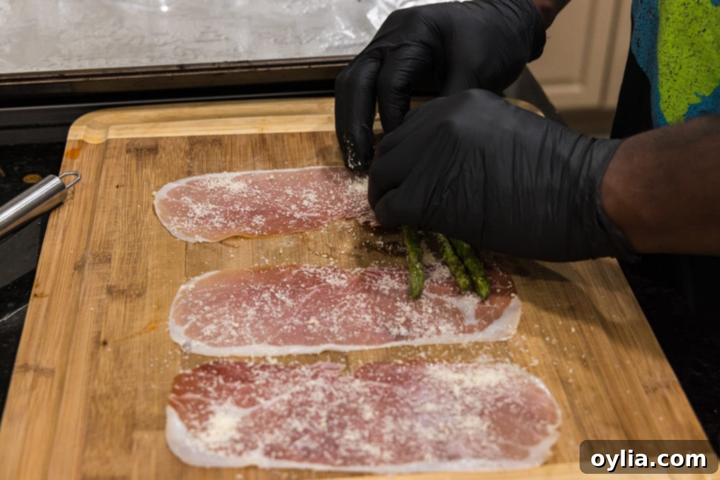 Hands carefully rolling a bundle of asparagus spears into a slice of prosciutto
