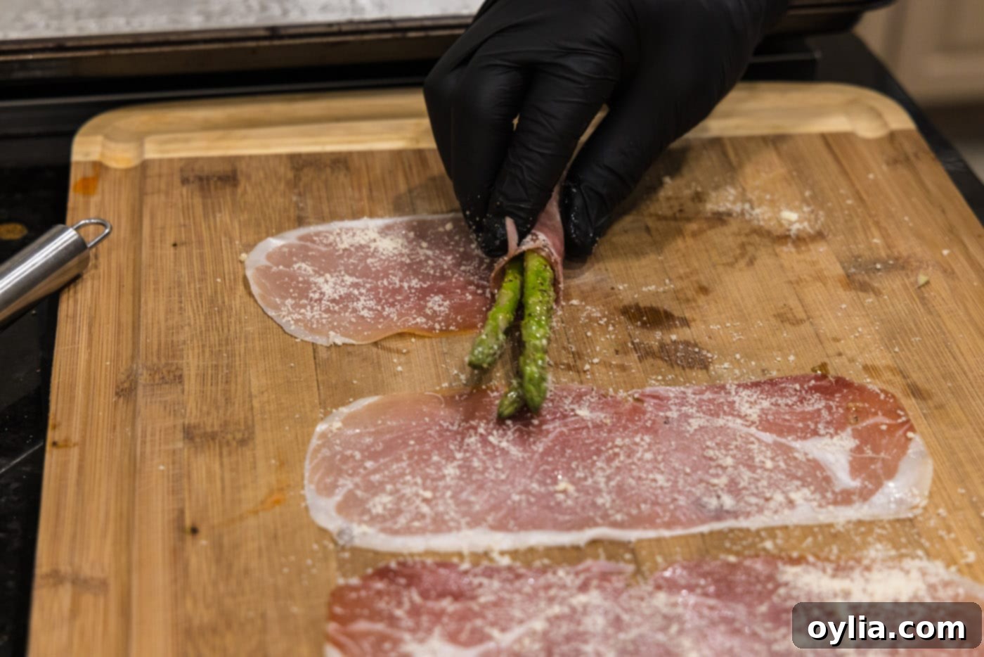 Close-up of asparagus spears being rolled in prosciutto, showcasing the technique