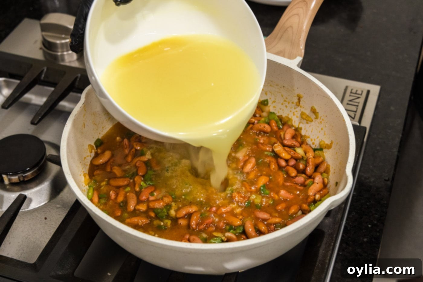 pouring chicken broth into skillet with red beans and sauteed vegetables