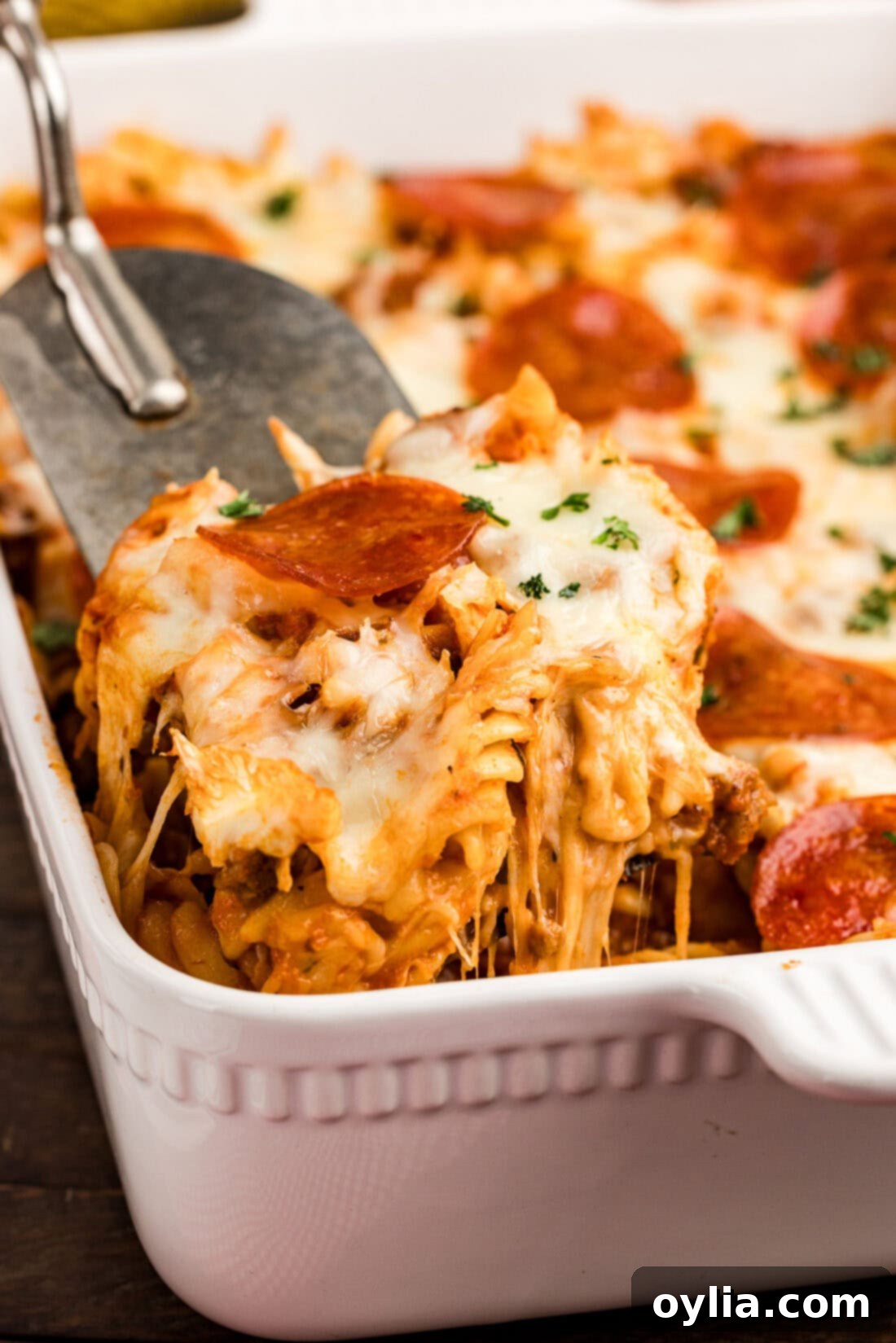 Hearty Sausage and Pepperoni Pizza Bake 3 Scoop of Sausage & Pepperoni Pizza Casserole being lifted out of the casserole dish, showing the layers of pasta, meat, and melted cheese