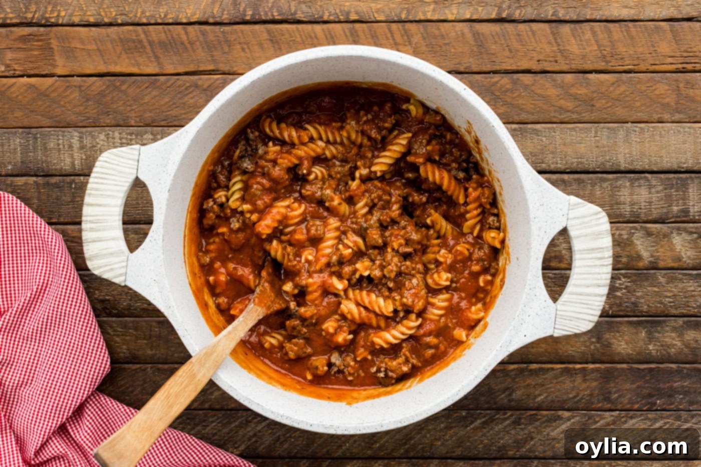 rotini pasta with marinara sauce and cooked sausage in a mixing bowl, before cheese and pepperoni are added
