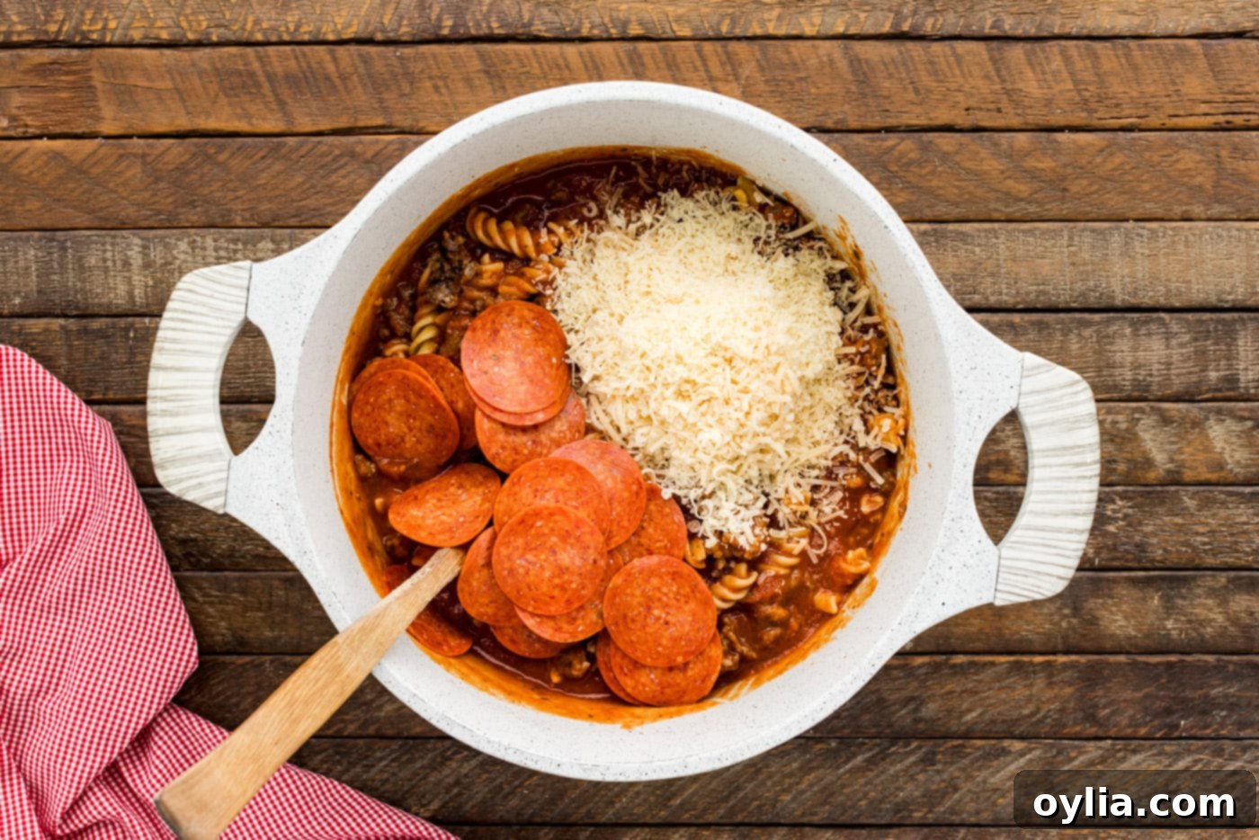 pepperoni and shredded Parmesan cheese being mixed into the pasta and sauce in a bowl