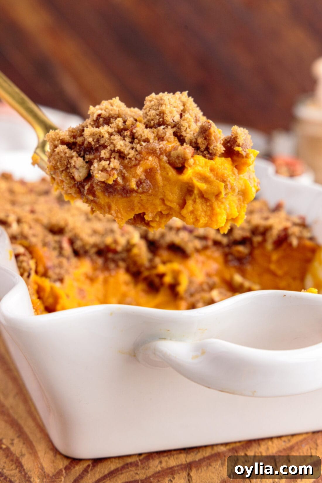 Spoonful of Sweet Potato Souffle being lifted out of the baking dish, showcasing its creamy texture and pecan streusel topping.