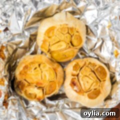 Close up photo of three bulbs of roasted garlic in foil