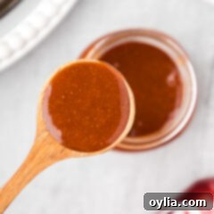 Close up photo of a spoon of Dr Pepper Barbecue Sauce held above a jar of Dr Pepper Barbecue Sauce, showcasing its perfect texture.