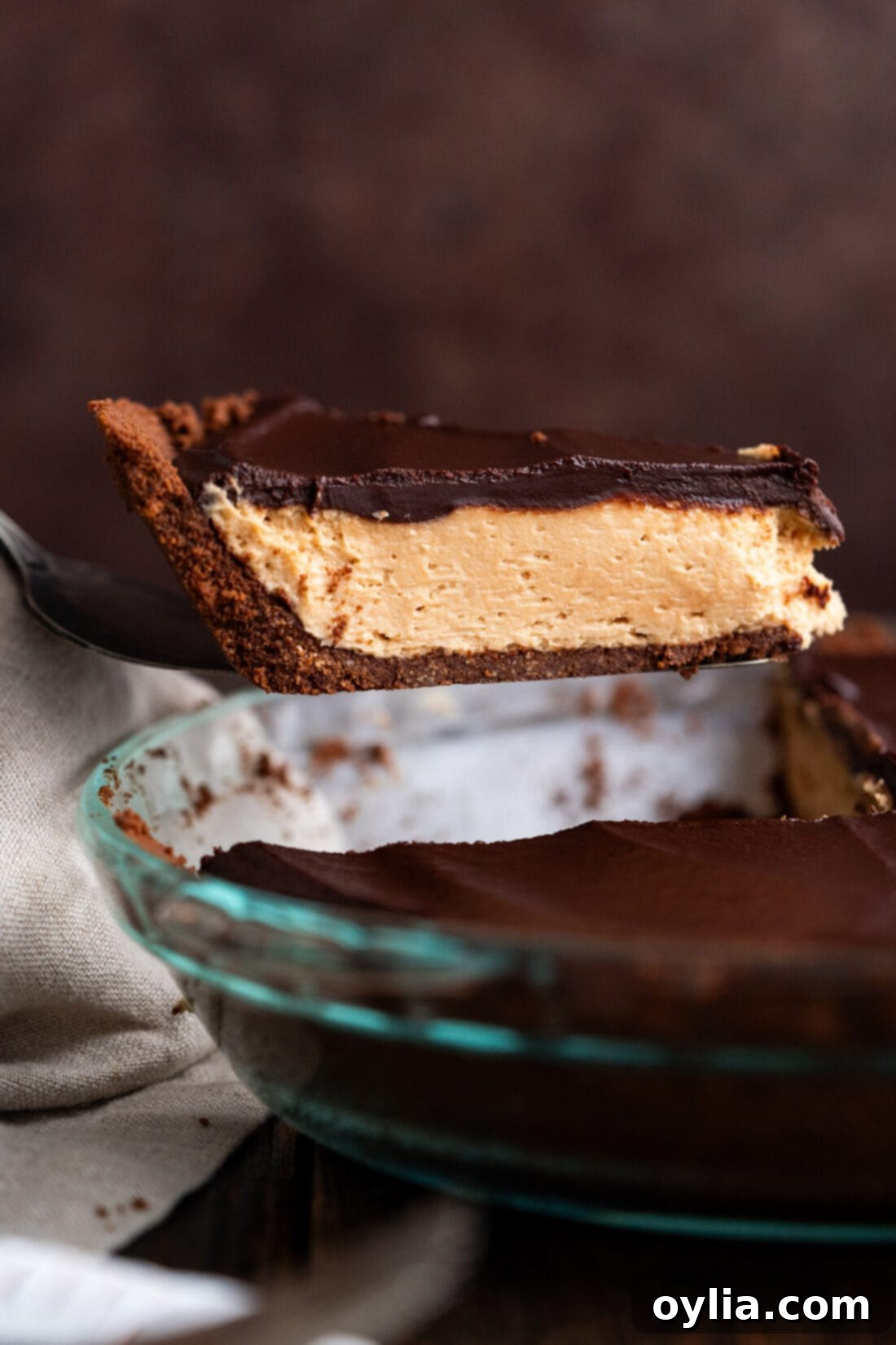 Rich Chocolate Peanut Butter Bliss 2 Slice of Chocolate Peanut Butter Pie being lifted out of the pie dish, showcasing its distinct layers of chocolate crust, creamy peanut butter filling, and shiny ganache topping.